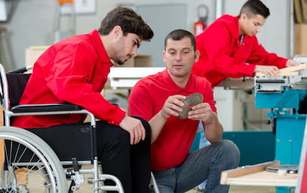 Un jeune apprenti en situation de handicap dans un atelier, en train d'écouter les explications de son tuteur. 