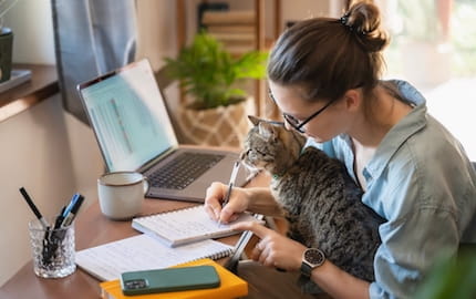 Une salarié·e en télétravail, qui écrit assise à son bureau avec son chat sur les genoux.