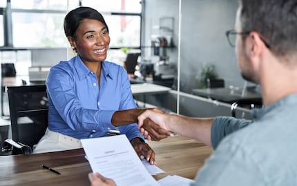 Une employeuse qui sert la main de sa nouvelle recrue, embauchée avec des coûts indirects de recrutement maîtrisés.